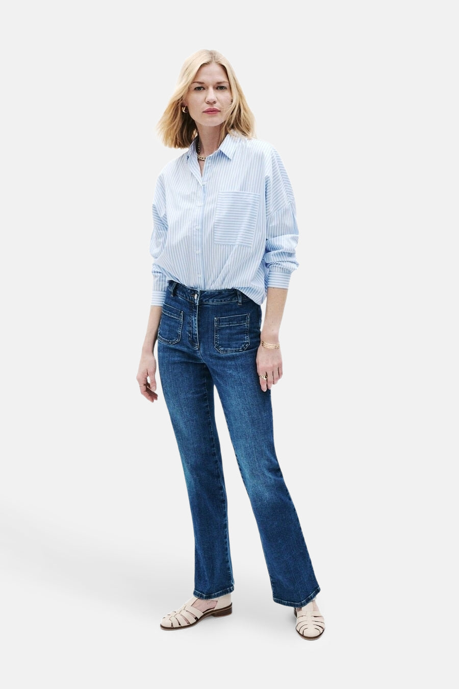 Jean bootcut bleu moyen de CAROLL, porté avec une chemise rayée bleue et blanche et des chaussures plates.

