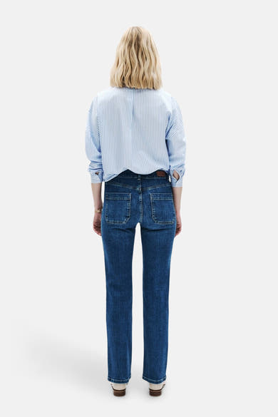 Jean bootcut bleu moyen de CAROLL, avec poches arrière rectangulaires et chemise rayée bleu et blanc.
