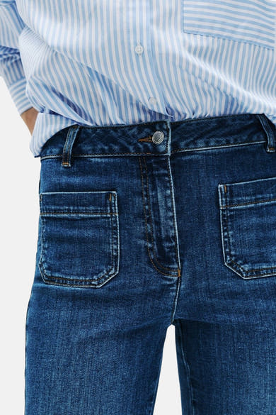 Jean bootcut en denim bleu moyen de CAROLL, avec poches plaquées avant et rayures sur la chemise portée.

