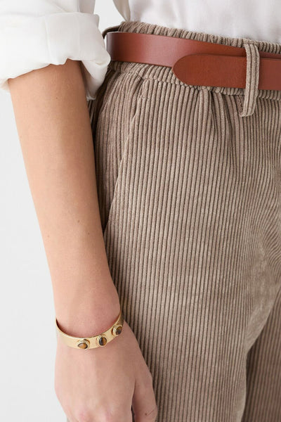Chino beige de CAROLL avec une ceinture marron, porté avec une chemise blanche et un bracelet doré.
