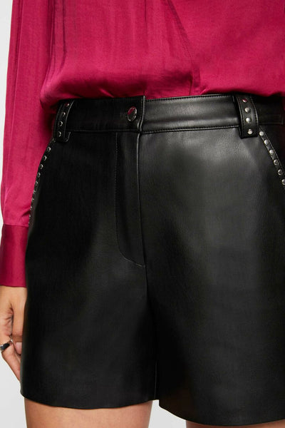 Short noir en similicuir de Morgan de Toi, orné de clous métalliques sur les côtés et porté avec un chemisier magenta.