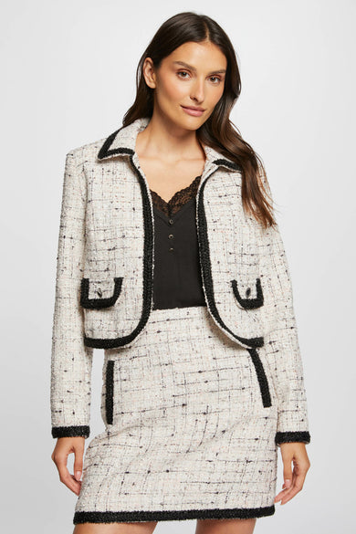 Veste courte blanche par Morgan de Toi, avec une texture tweed, des bordures noires et des poches plaquées.
