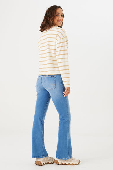 Jean évasé bleu moyen de GARCIA, avec coupe bootcut, porté avec un haut rayé et des chaussures de sport.