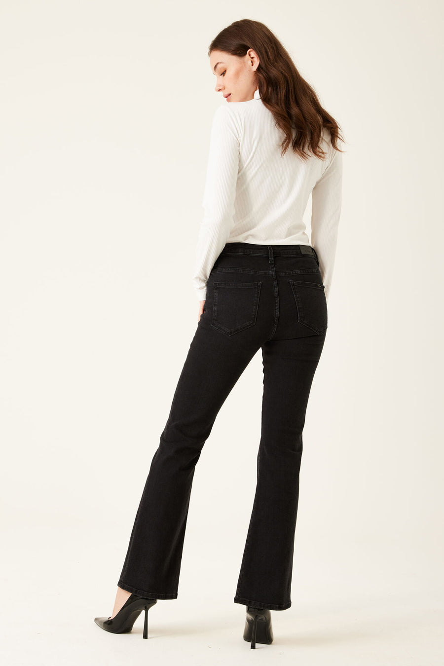 Jeans évasés noirs en denim par GARCIA, portés avec un haut blanc à manches longues et des escarpins noirs.
