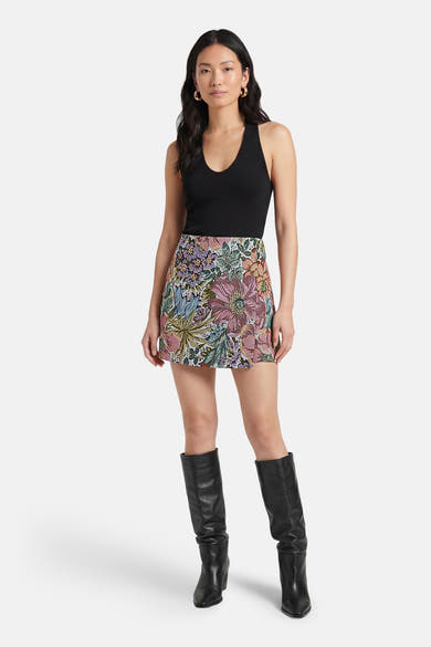 Short multicolore Terra di Siena avec un motif floral, porté avec un haut noir et des bottes en cuir noir.
