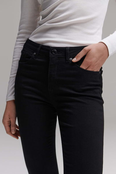 Jean slim noir d'OPUS, porté avec un haut à manches longues blanc et une main dans la poche.