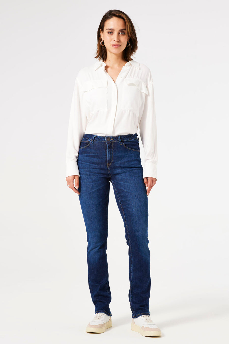 Jean droit en denim bleu foncé de GARCIA, porté avec une chemise blanche à manches longues et des baskets crème et blanches.
