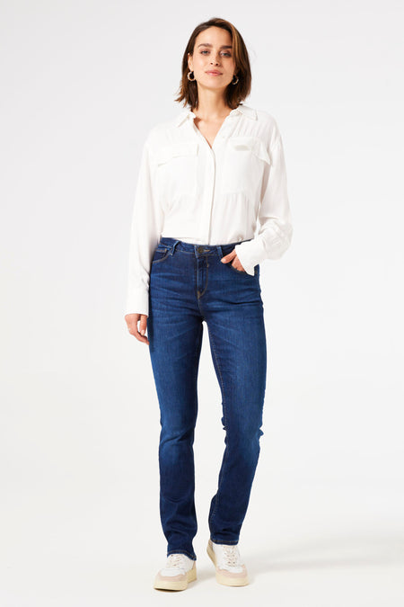 Jean droit bleu foncé de GARCIA, porté avec une chemise blanche à manches longues et des baskets.
