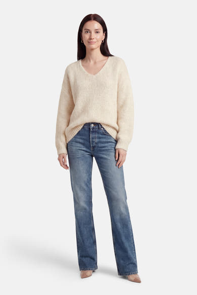 Pull à col en V écru de Terra di Siena, porté avec un jean bleu et des escarpins nude.
