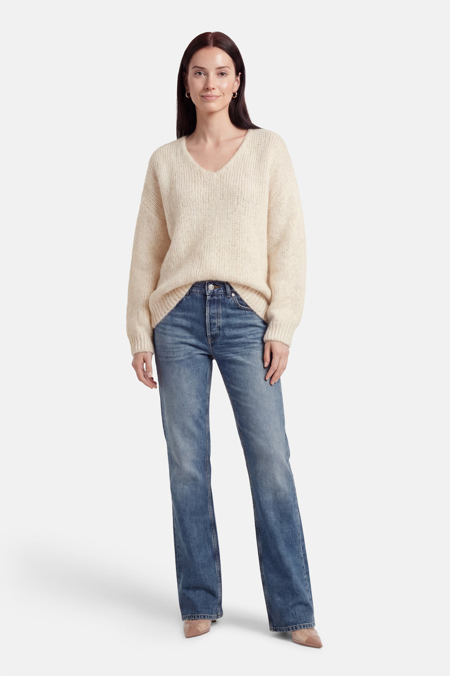 Pull à col en V écru de Terra di Siena, porté avec un jean bleu et des escarpins nude.