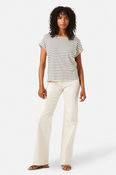 Jean large en denim blanc cassé de GARCIA, porté avec un t-shirt rayé noir et blanc et des sandales dorées.