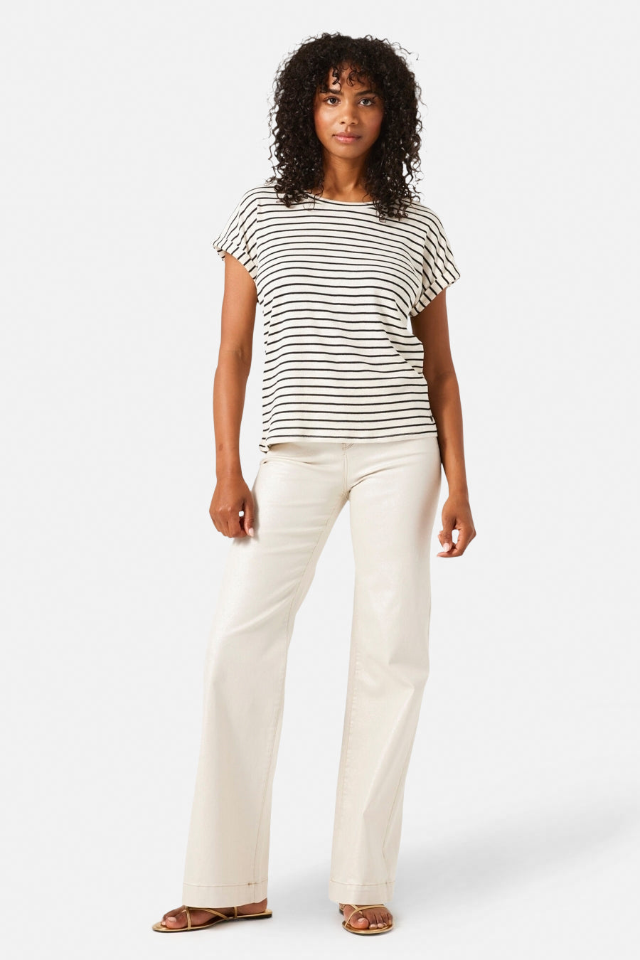 Jean large en denim blanc cassé de GARCIA, porté avec un t-shirt rayé noir et blanc et des sandales dorées.