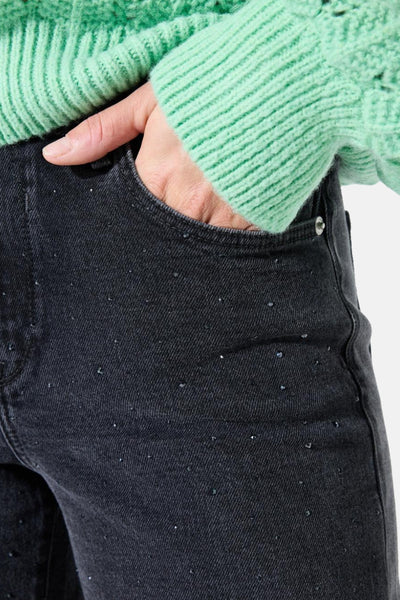 Jean large en denim noir de GARCIA, orné de petits strass, avec une main dans la poche.
