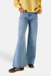Jean large denim bleu clair de GARCIA, effet scintillant, coupe évasée, porté avec cardigan jaune et baskets.