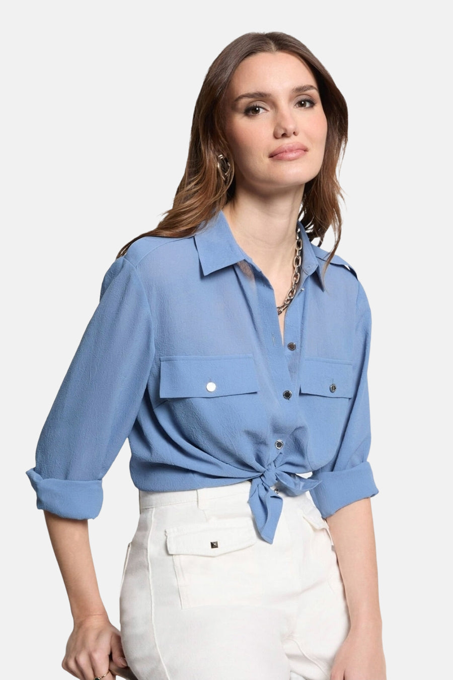 Blauwe blouse met lange mouwen van Morgan de Toi, met zakken, geknoopt aan de voorkant, gedragen met een witte broek.