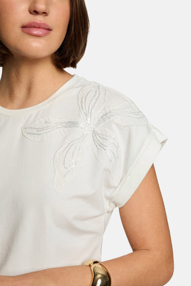 T-shirt blanc à manches courtes de Morgan de Toi avec une fleur décorative argentée sur l'épaule.