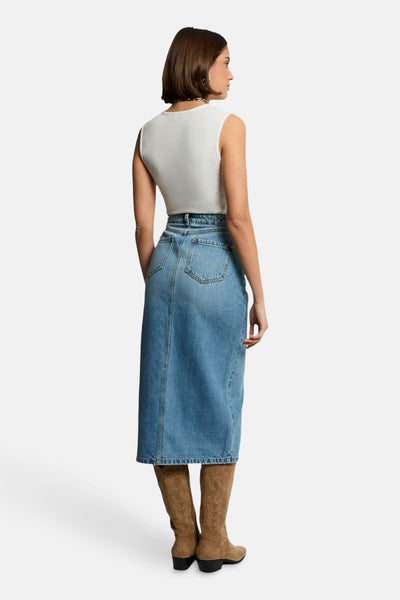 Top blanc sans manches de Morgan de Toi, porté avec une jupe longue en denim et des bottes marron.
