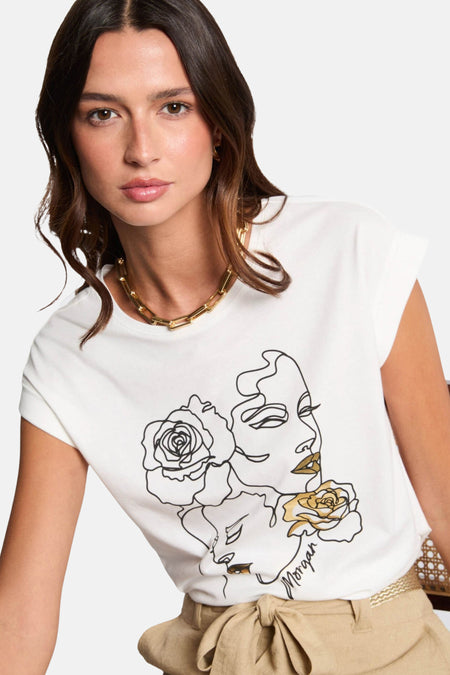 T-shirt blanc à manches courtes de Morgan de Toi, avec dessin de visage et fleurs, porté avec un collier doré.