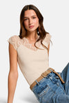 Top sans manches beige de Morgan de Toi, avec dentelle au col en V, porté avec un jean et une ceinture marron.
