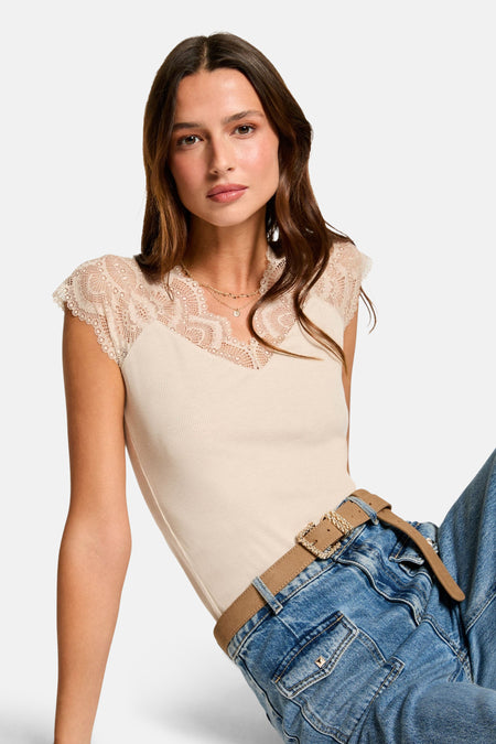Top sans manches beige de Morgan de Toi, avec dentelle au col en V, porté avec un jean et une ceinture marron.
