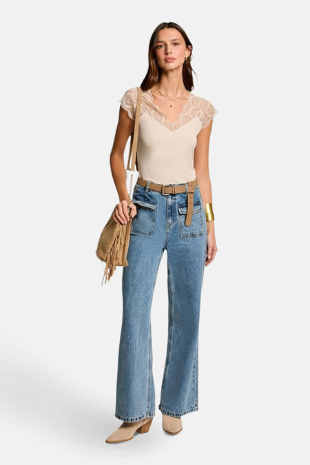 Top sans manches beige de Morgan de Toi avec dentelle au décolleté, porté avec un jean taille haute et une ceinture.
