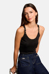 Zwarte top van Morgan de Toi, met pailletten, gedragen met een donkerblauwe wijde jeans, een gouden manchetarmband en zwarte pumps.