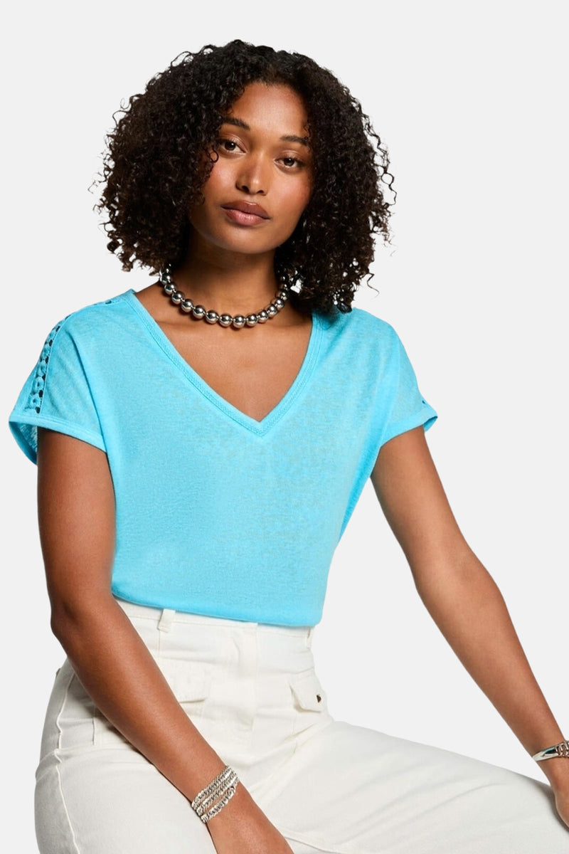 T-shirt bleu à manches courtes de Morgan de Toi avec détail ajouré à l'épaule, porté avec un collier et des bracelets argentés.