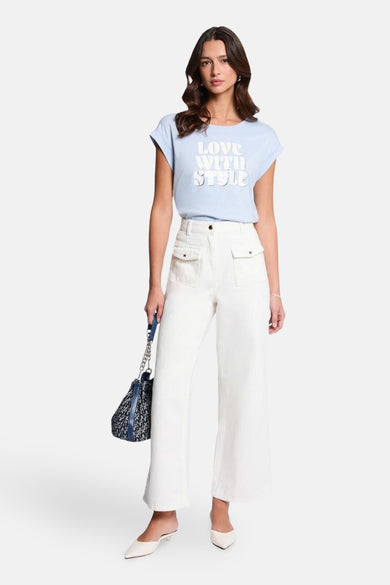 T-shirt bleu clair à manches courtes de Morgan de Toi avec inscription blanche, porté avec un pantalon blanc taille haute.

