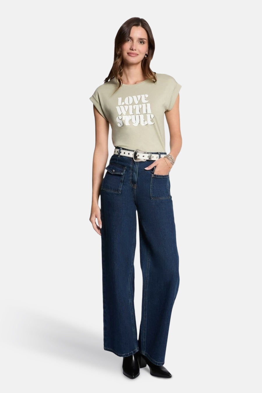 T-shirt à manches courtes vert de Morgan de Toi, avec inscription blanche, porté avec un jean taille haute et une ceinture blanche.
