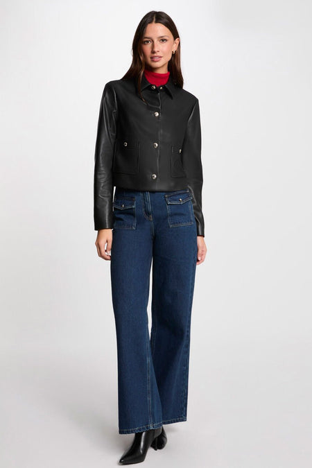 Veste courte noire de Morgan de Toi, avec poches plaquées et boutons argentés, portée avec un jean bleu.
