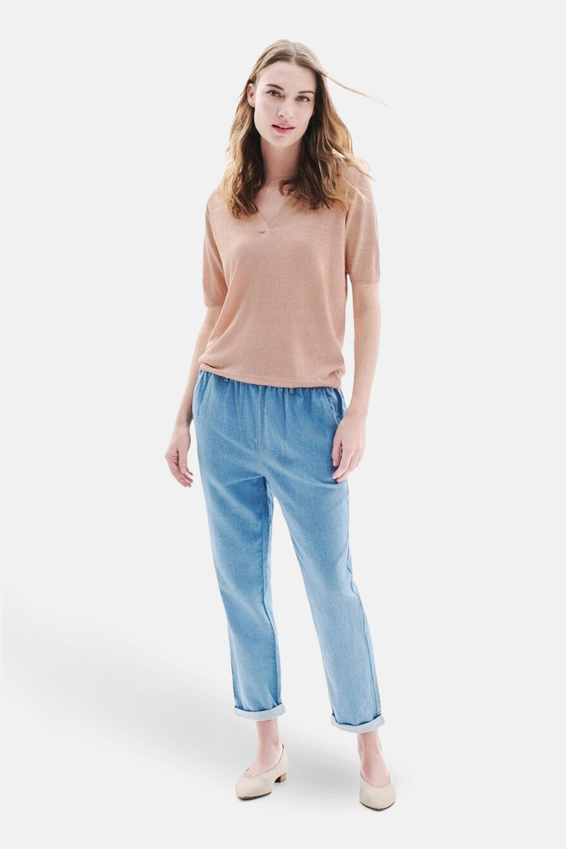 Polo rose à manches courtes de CAROLL, porté avec un pantalon bleu décontracté et des chaussures plates.
