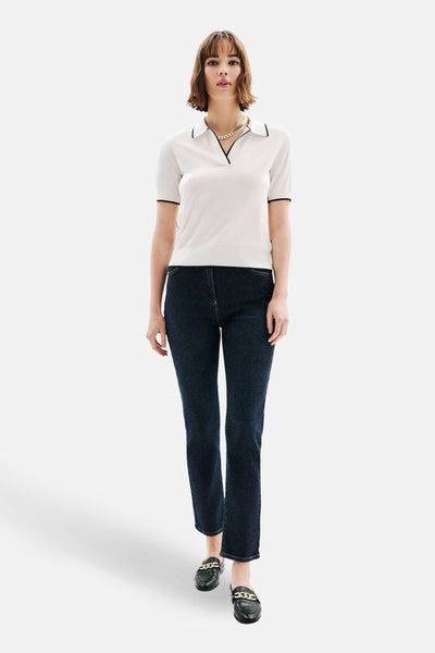 Polo blanc à manches courtes de Caroll, avec bordure noire au col et aux manches, porté avec un jean foncé.