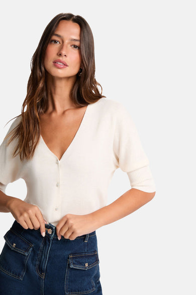 Cardigan écru de Morgan de Toi avec manches courtes et boutons décoratifs, porté avec un jean taille haute.
