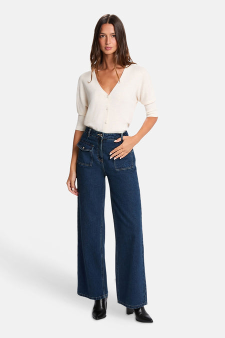 Cardigan écru de Morgan de Toi à col V, boutons, manches courtes bouffantes, porté avec un jean bleu foncé taille haute à poches et bottines noires.