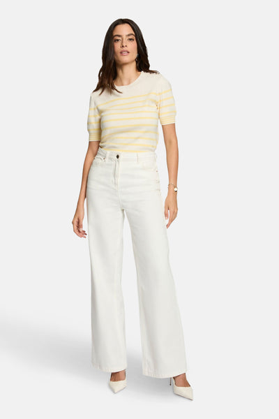 Multikleuren gestreepte rondehals-trui van Morgan de Toi, gedragen met een witte broek met hoge taille en witte pumps.