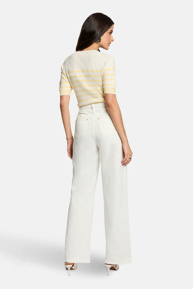 Pull à col rond multicolore de Morgan de Toi avec des rayures horizontales, porté avec un pantalon blanc et des escarpins.