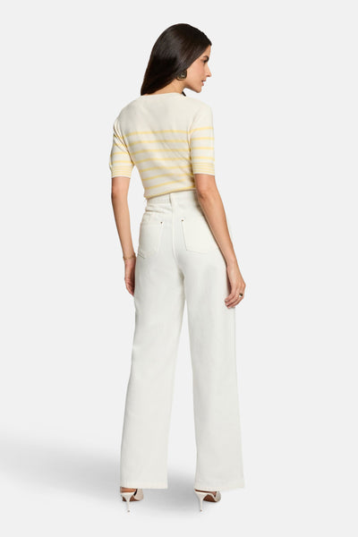Pull à col rond multicolore de Morgan de Toi avec des rayures horizontales, porté avec un pantalon blanc et des escarpins.