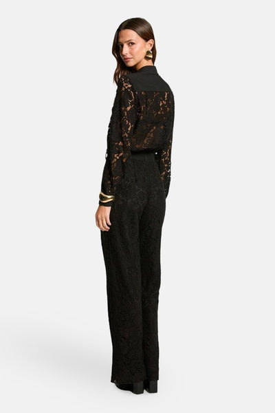 Zwarte kanten jumpsuit van Morgan de Toi, met klassieke kraag en lange mouwen, gedragen met gouden oorbellen.