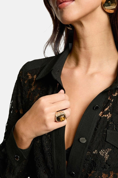 Zwarte jumpsuit van Morgan de Toi, met bloemenkant op een vrouw met een gouden ring en oorbellen.