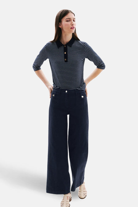 Jean coloré bleu de CAROLL, large et droit, avec des boutons dorés, porté avec un polo rayé.
