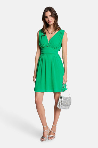 Robe courte verte de Morgan de Toi, avec encolure en V, portée avec des sandales argentées et un sac à main argenté.