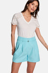 Short bleu de Morgan de Toi avec ceinture тон sur тон et plis, porté avec un tee-shirt blanc à manches ajourées.