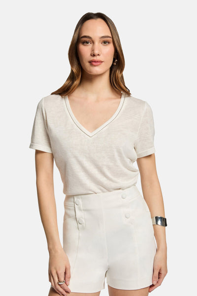 White high-waisted shorts with front button details, worn with a cream V-neck top and silver cuff bracelet, front view.