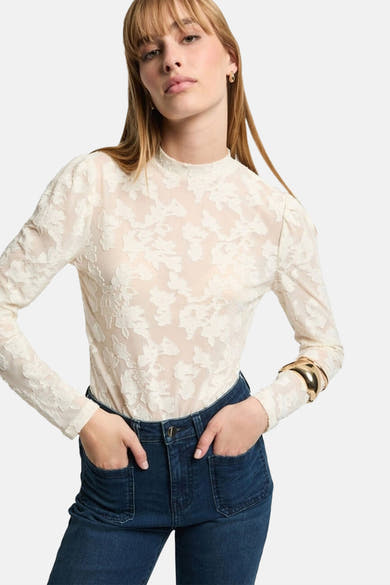 T-shirt à manches longues blanc en dentelle by Morgan de Toi porté avec un jean bleu et un bracelet doré.
