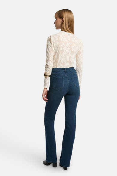 T-shirt blanc à manches longues de Morgan de Toi, avec un motif floral en dentelle et porté avec un jean bleu.
