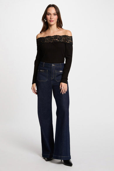 T-shirt noir à manches longues de Morgan de Toi, avec dentelle sur les épaules, porté avec un jean évasé bleu foncé.
