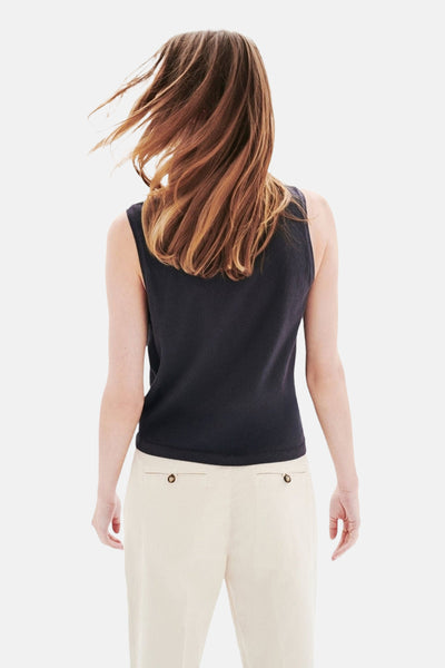 Top sans manches gris par CAROLL, porté avec un pantalon beige, dos visible, cheveux châtains au vent.
