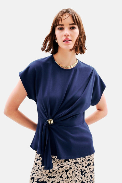 Blauwe T-shirt van CAROLL met een gedrapeerd effect, een gouden ring en een subtiel bloemenpatroon aan de onderkant.