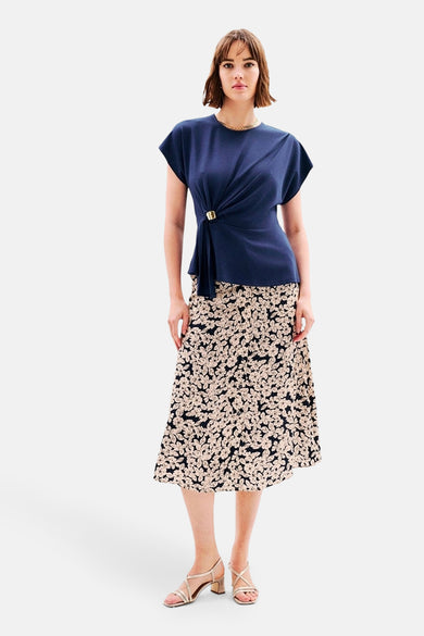 T-shirt bleu CAROLL avec un nœud et une boucle décorative, porté avec une jupe à motifs floraux.
