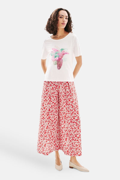 T-shirt à manches courtes blanc de CAROLL, avec motif floral devant, porté avec un pantalon fleuri rouge.

